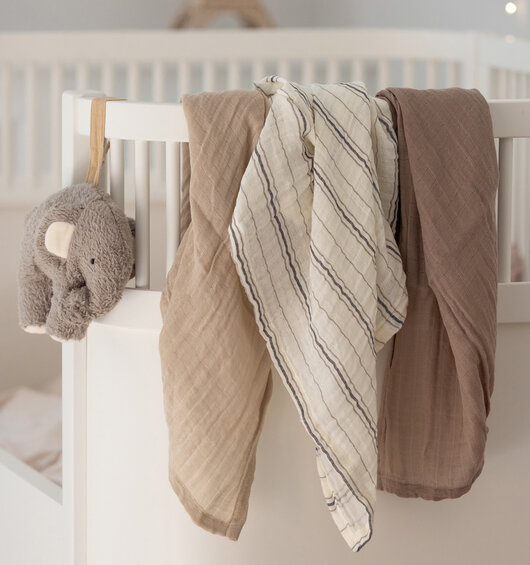 En fin hvid barneseng hvor der hænger 3 stofbleer over kanten på sengen